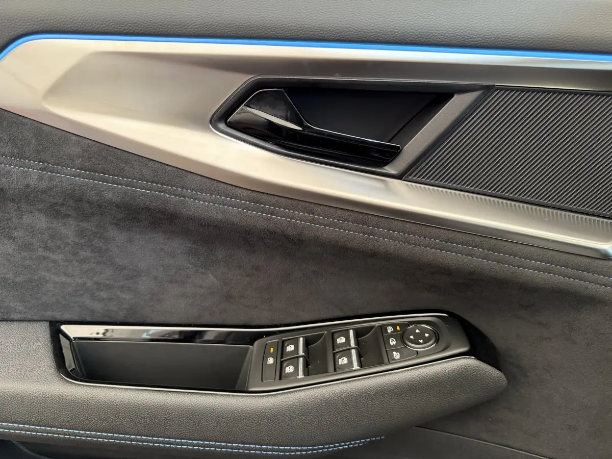 Gros plan sur la porte côté gauche du Renault Espace gris foncé esprit Alpine, avec commandes de vitres et surpiqûres bleues.