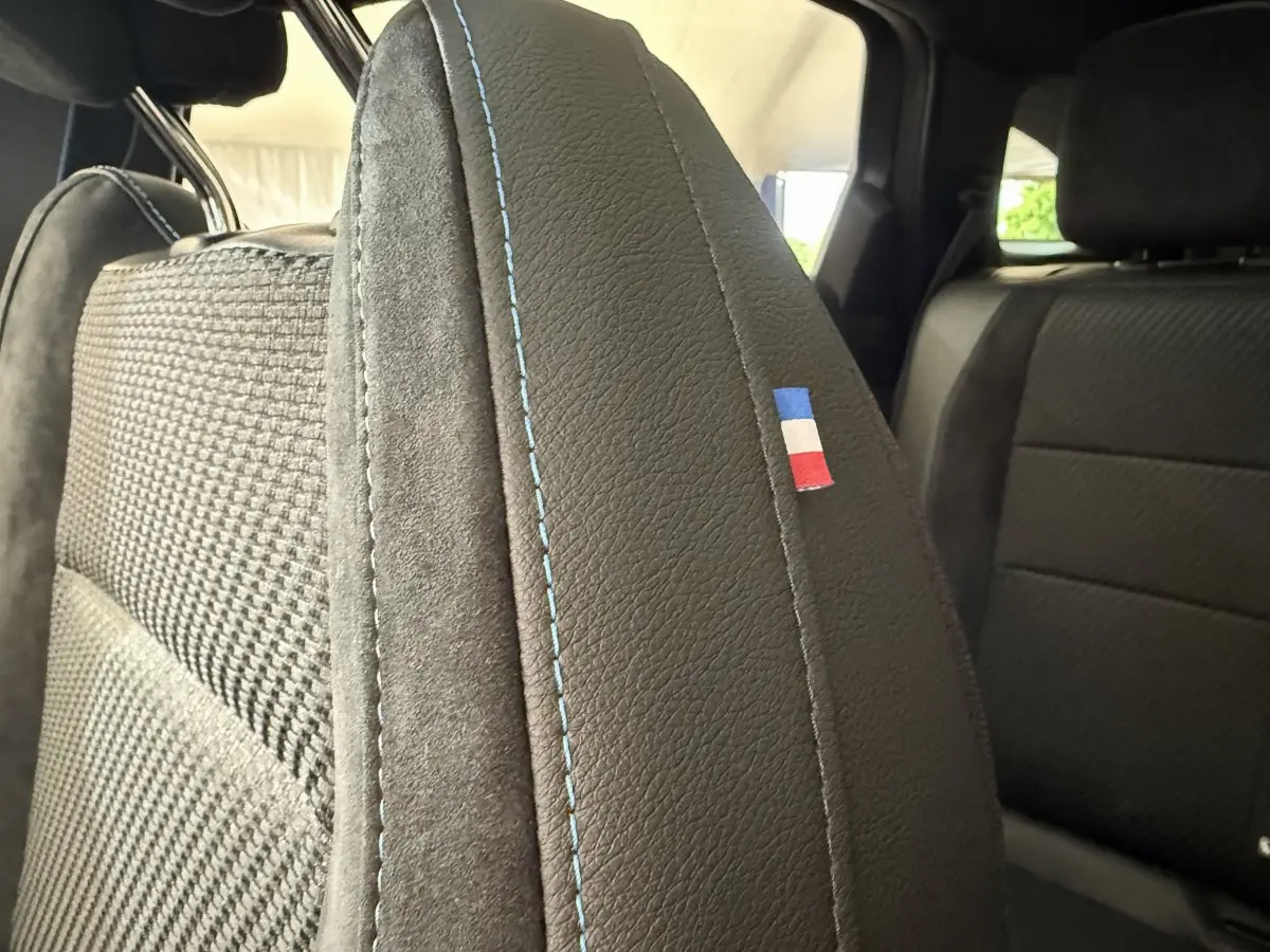 Gros plan sur la couture bleue et le drapeau tricolore du siège avant côté gauche du Renault Espace gris foncé esprit Alpine.