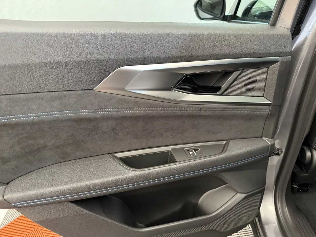 Gros plan sur la porte intérieure côté droit du Renault Espace gris foncé esprit Alpine 7PL avec surpiqûres bleues et poignée argentée.