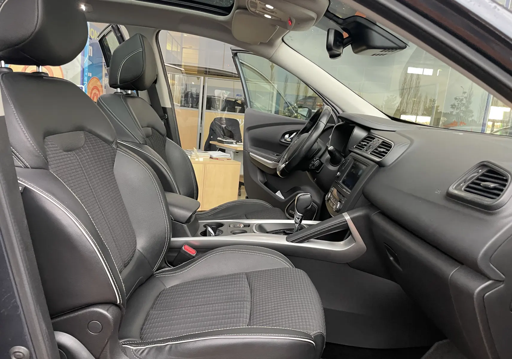 Intérieur avant droit du Renault Kadjar gris titanium 2018, sièges tissu noir avec surpiqûres blanches et tableau de bord moderne.