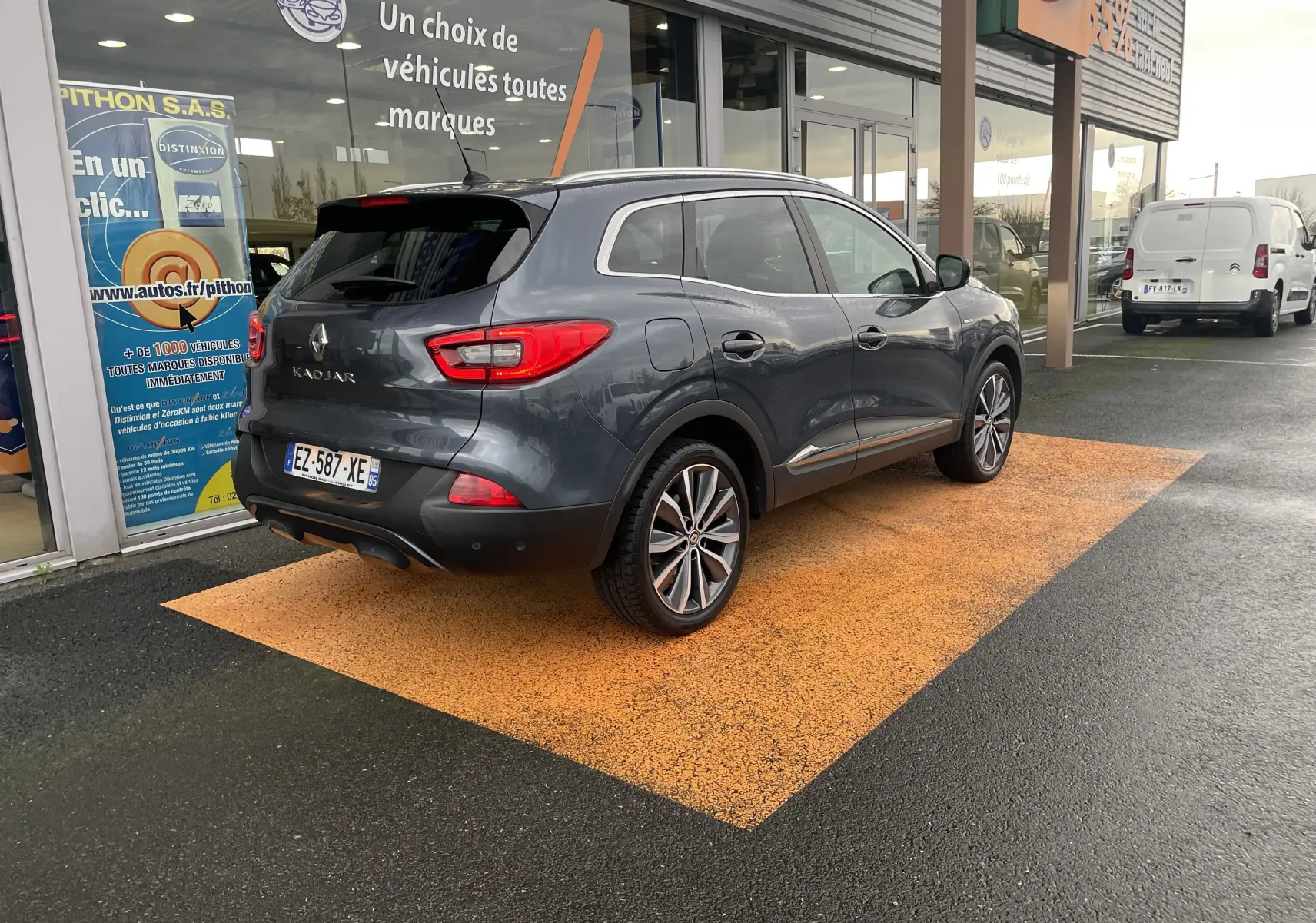 Renault Kadjar gris titanium vu en 3/4 arrière droit, stationné devant un showroom avec jantes bi-ton et feux LED.