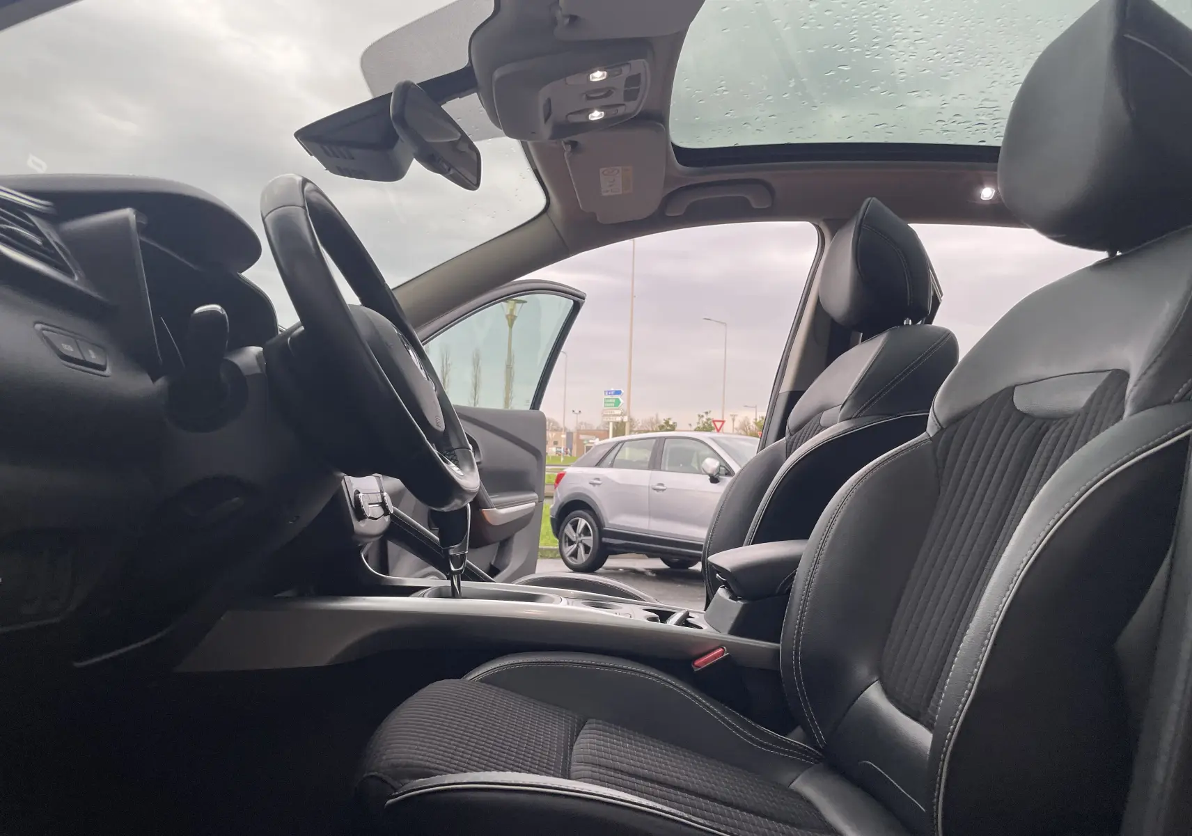 Vue intérieure côté conducteur du Renault Kadjar 2018, sièges en tissu noir et toit panoramique visible.