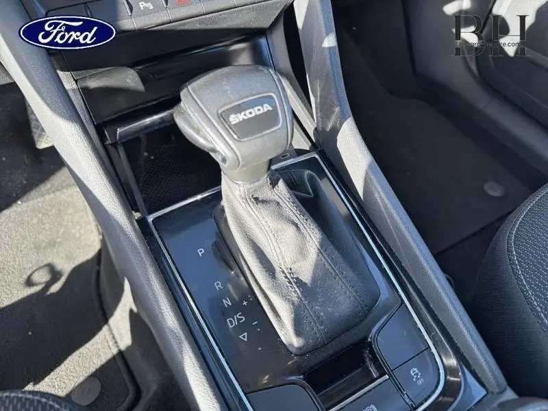 Gros plan sur le levier de vitesses automatique noir avec logo ŠKODA, entouré de la console centrale intérieure.