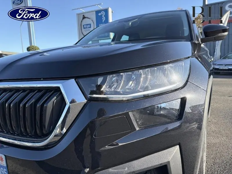 Gros plan sur l'avant droit d'un Skoda Kodiaq noir Magic Nacré, mettant en valeur le phare et la calandre chromée.