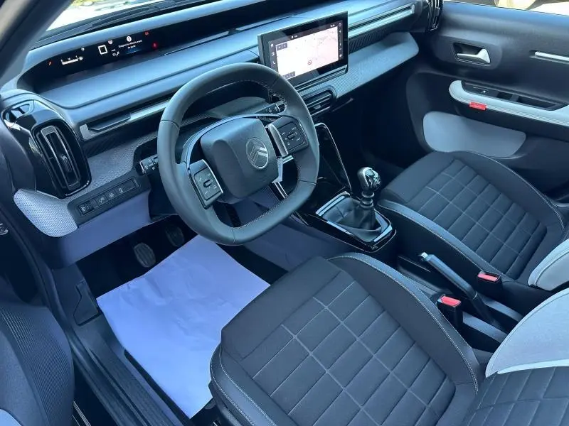 Vue intérieure côté conducteur de la Citroën C3 2025, avec tableau de bord noir, volant multifonctions et sièges tissu noir.