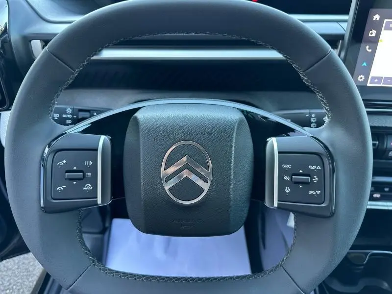 Vue rapprochée du volant noir de la Citroën C3 1.2 Turbo 100ch PLUS avec commandes intégrées et logo chromé central.