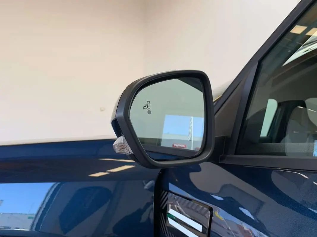 Rétroviseur côté gauche du Dacia Bigster bleu indigo avec toit noir, montrant l'alerte d'angle mort intégrée.