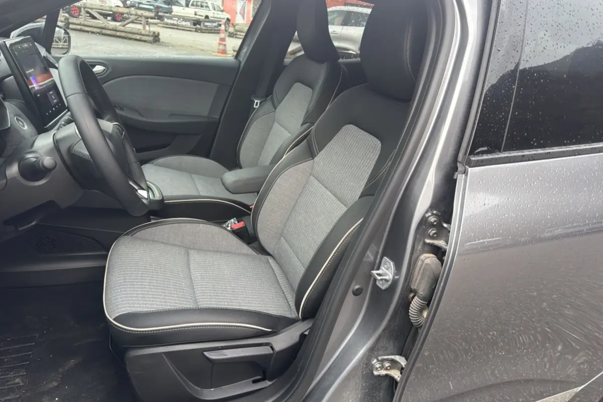 Vue intérieure côté conducteur de la Renault Clio gris schiste 2025, montrant les sièges avant en tissu et cuir avec volant multifonctions.