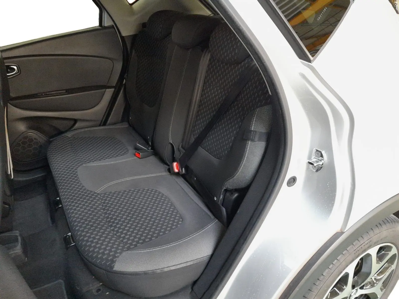 Vue côté droit arrière du Renault Captur gris clair métal, montrant l’ouverture de porte et la banquette arrière en tissu noir.