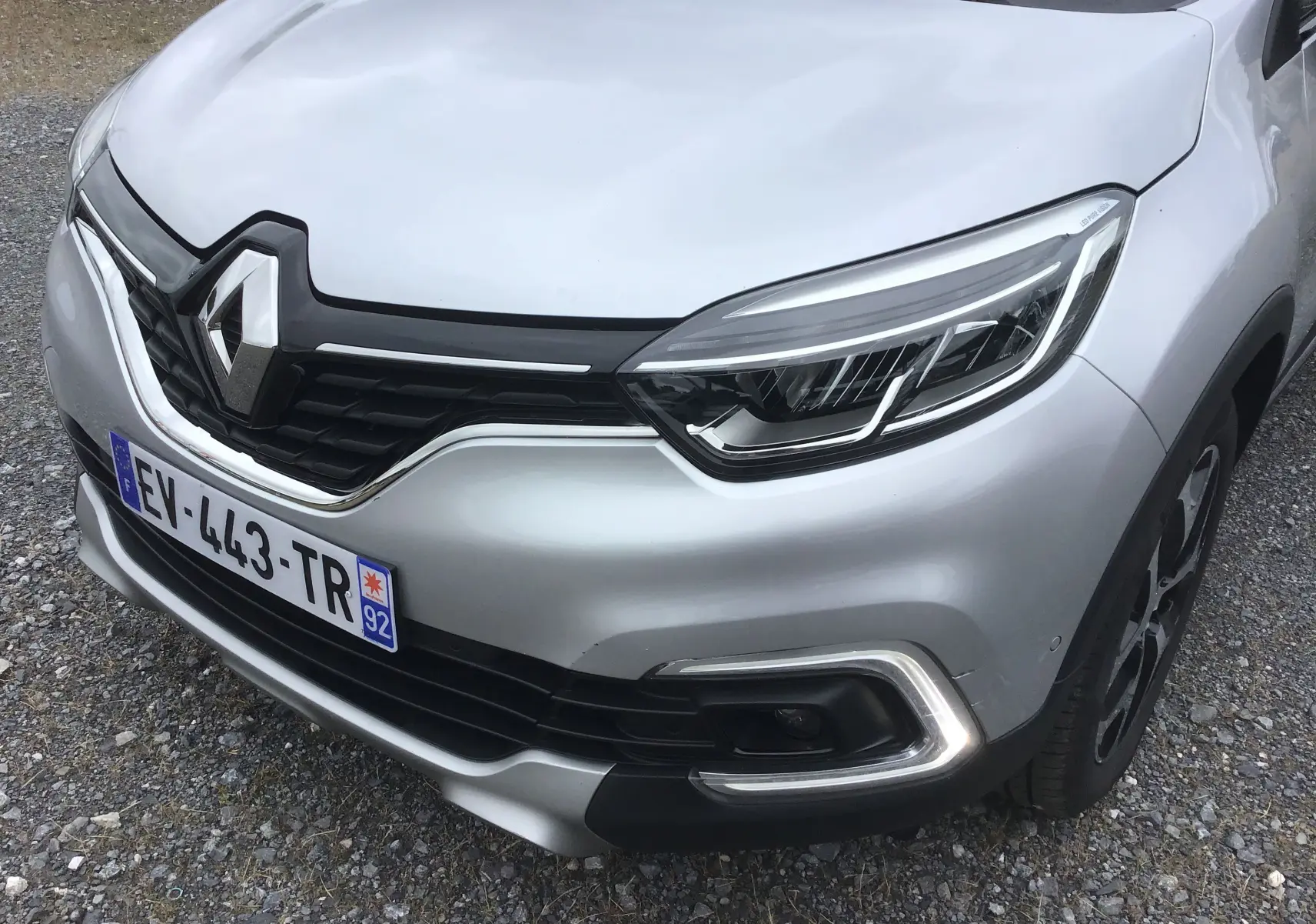 Vue 3/4 avant droit du Renault Captur gris clair métal avec calandre noire et signature lumineuse LED distinctive.