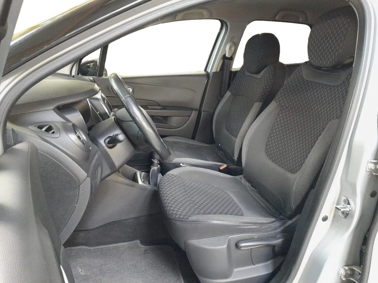 Vue intérieure côté conducteur du Renault Captur gris clair, montrant les sièges avant en tissu noir et la console centrale.