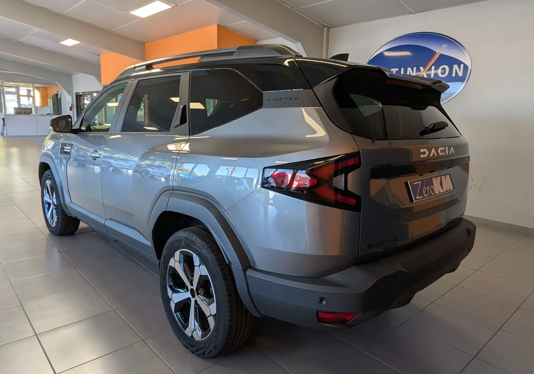 Vue 3/4 arrière droite du Dacia Bigster gris schiste avec toit bi-ton noir et jantes alliage diamantées en showroom.