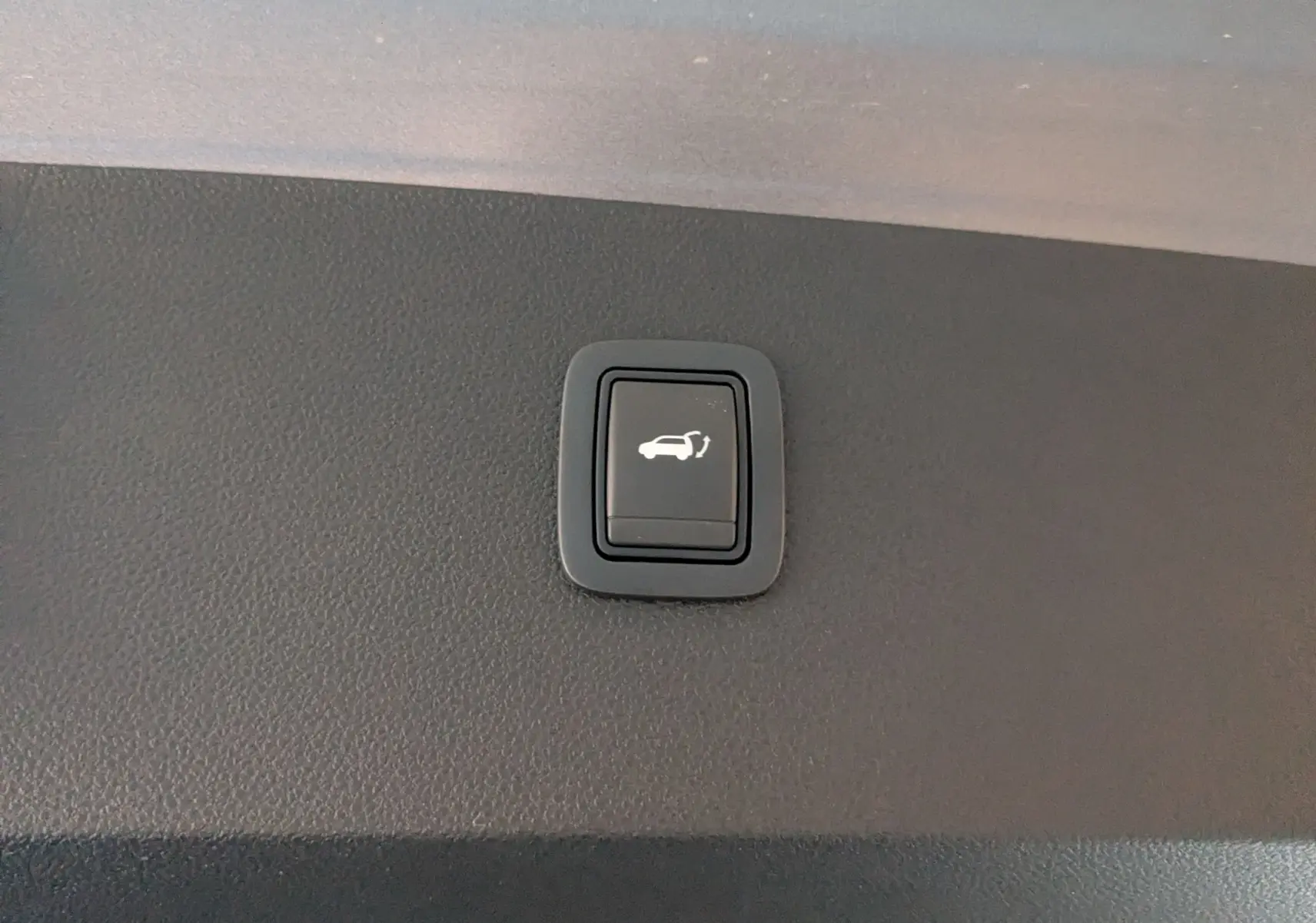 Bouton noir d'ouverture électrique du hayon sur la garniture intérieure du coffre du Dacia Bigster gris schiste.