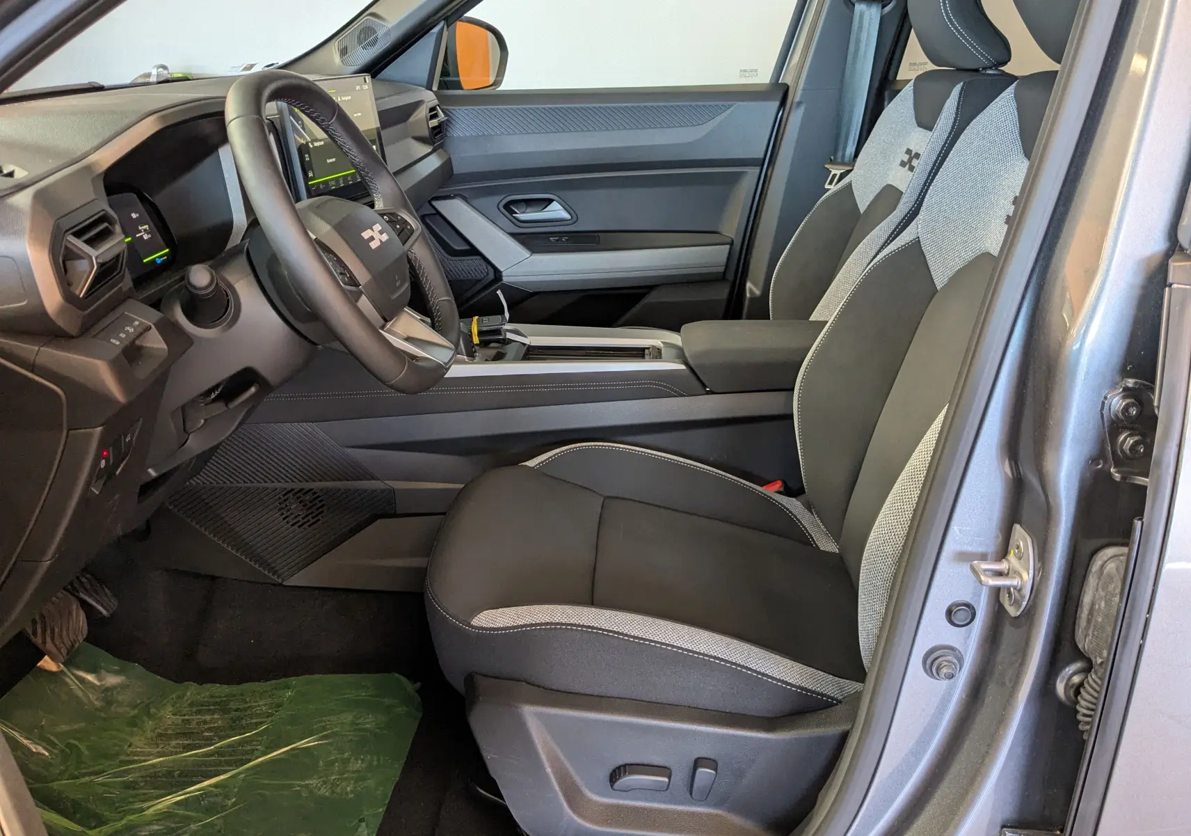 Vue intérieure côté conducteur du Dacia Bigster Hybrid 155 Journey gris schiste, mettant en valeur le tableau de bord moderne et les sièges bicolores.