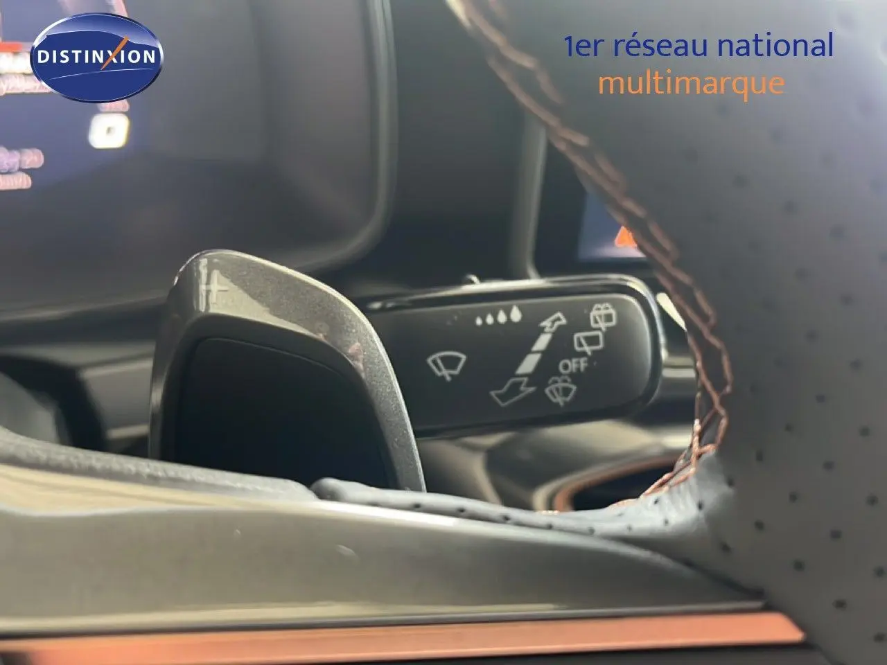 Gros plan sur la palette de changement de vitesse et la commande d’essuie-glace derrière le volant en cuir perforé brun.