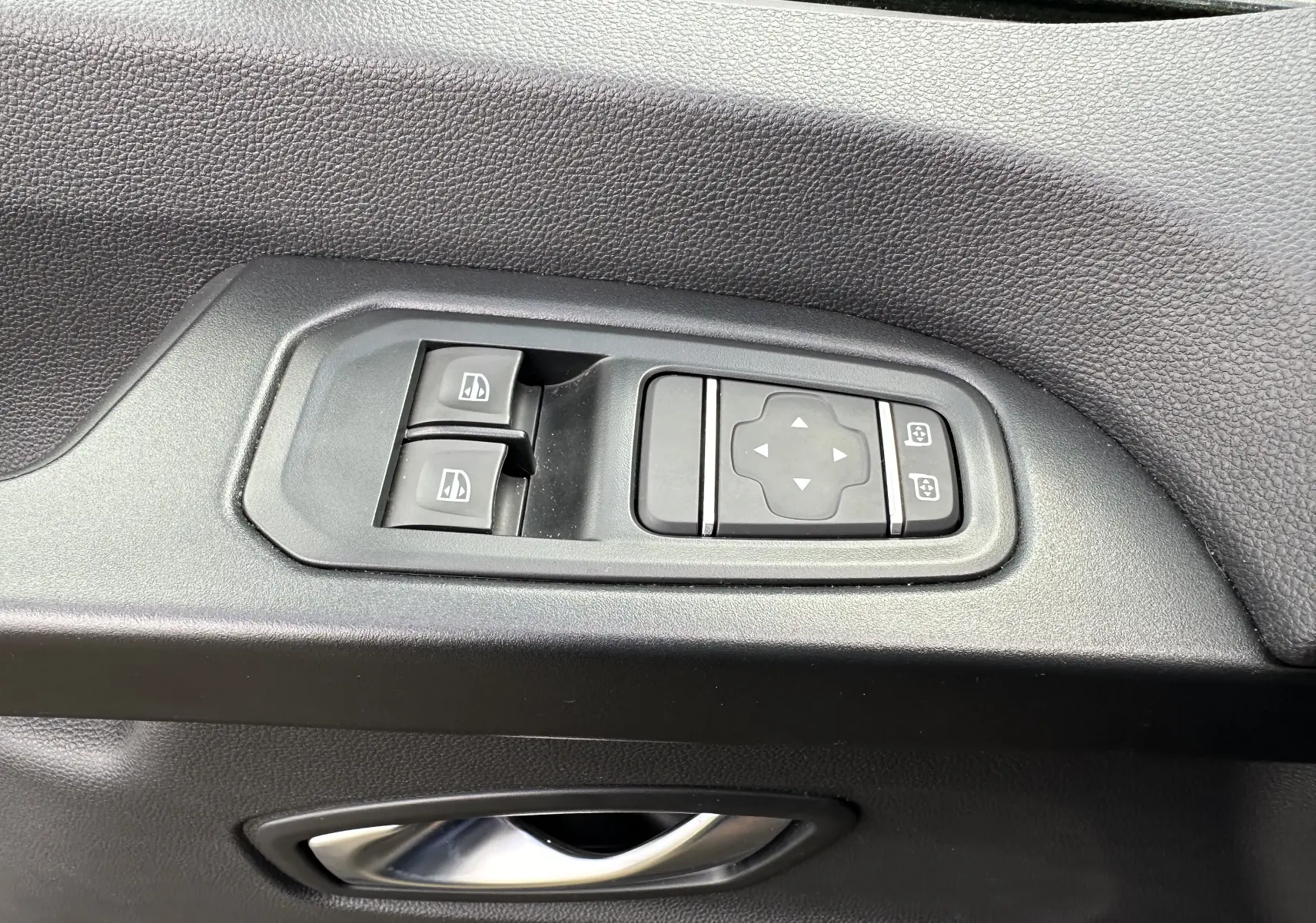 Détail des commandes de lève-vitres et réglage des rétroviseurs sur la portière intérieure noire du Renault Trafic Combi gris Comète 2023.