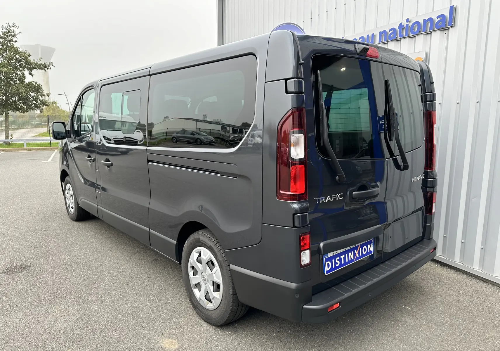 Renault Trafic Combi gris comète vu en 3/4 arrière droit, soulignant ses grandes vitres teintées et portes arrière battantes.