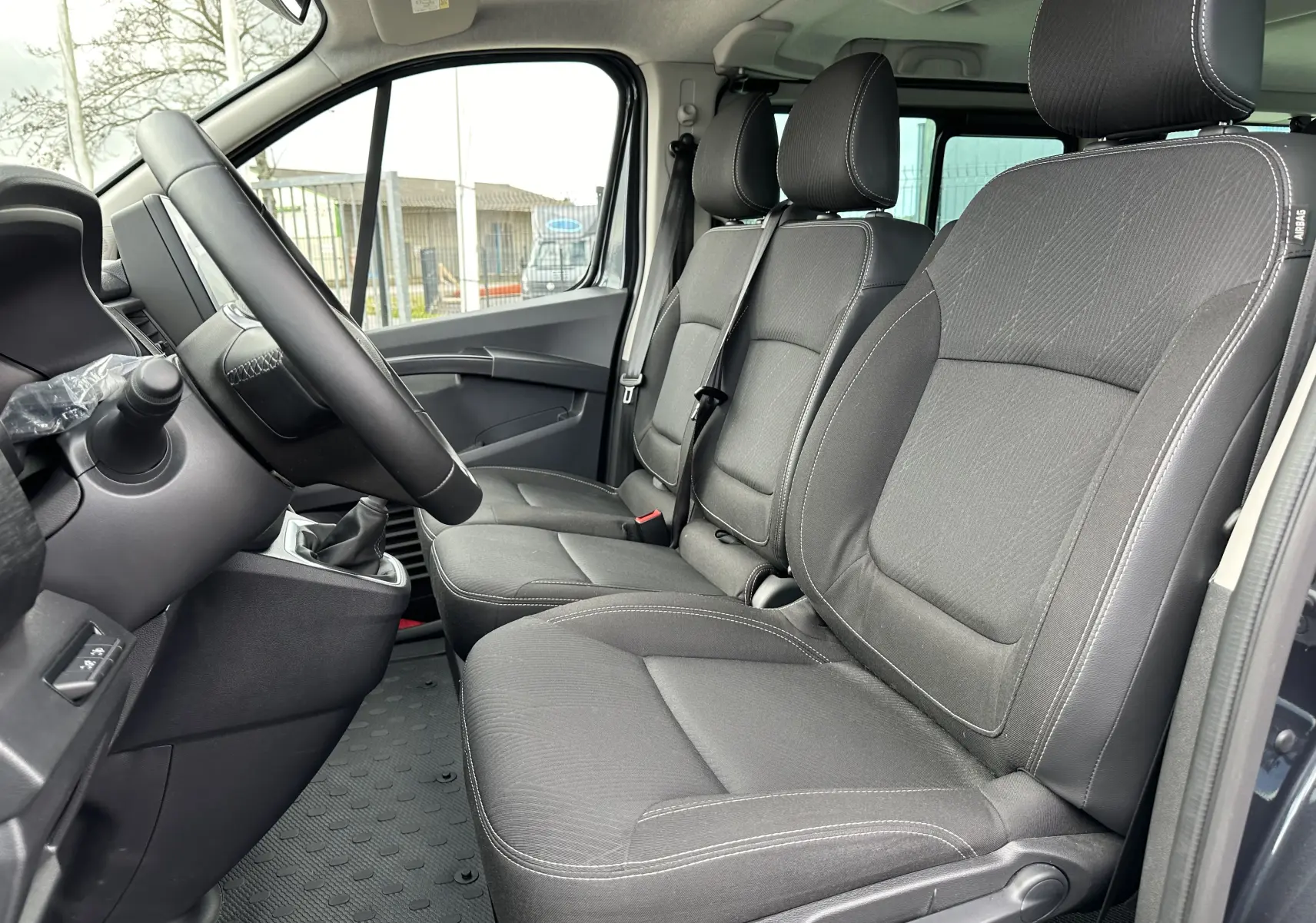 Vue intérieure côté conducteur du Renault Trafic Combi 2023, sièges tissu noir avec coutures blanches visibles.
