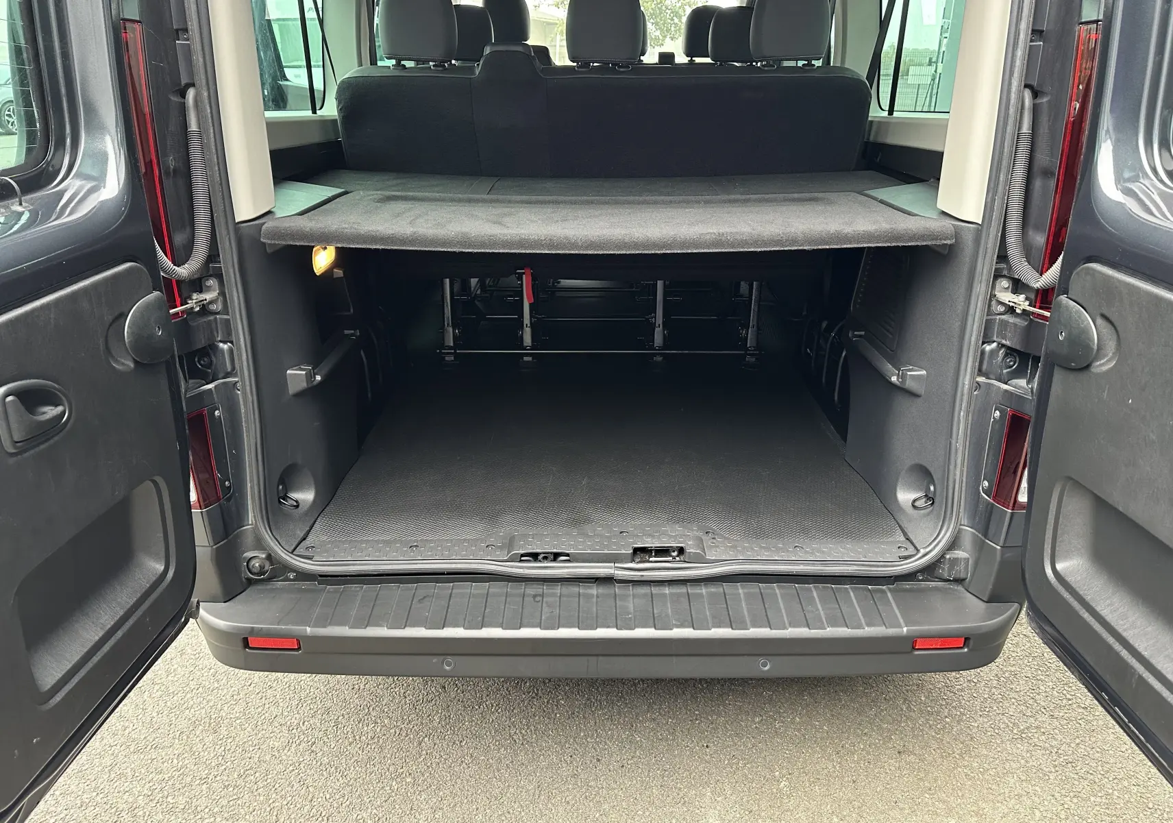 Vue arrière du Renault Trafic Combi gris comète 2023 avec portes ouvertes et espace de chargement visible.