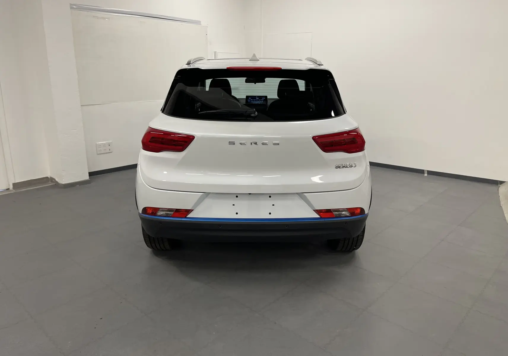 Vue arrière du SUV électrique blanc SERES 3 Luxury, avec feux rouges et vitres arrière teintées dans un garage.