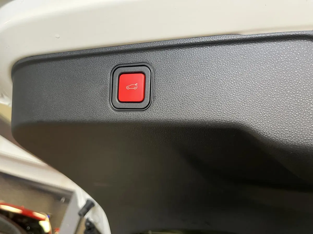 Bouton rouge d'ouverture électrique du hayon sur le bord intérieur du coffre d'une FIAT 600 blanche 2024.