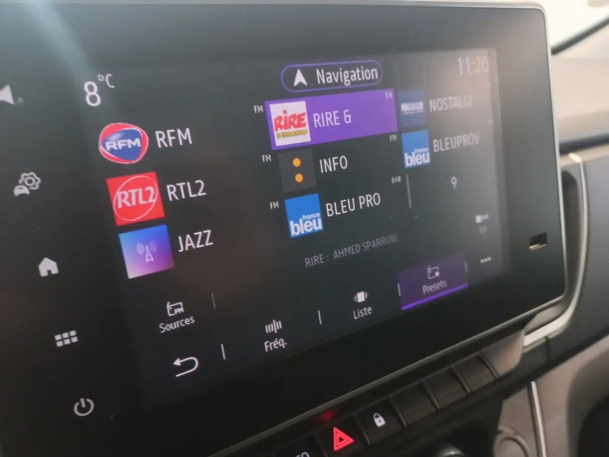 Écran tactile central du tableau de bord du Renault Trafic Fourgon blanc, affichant les stations radio et la navigation.