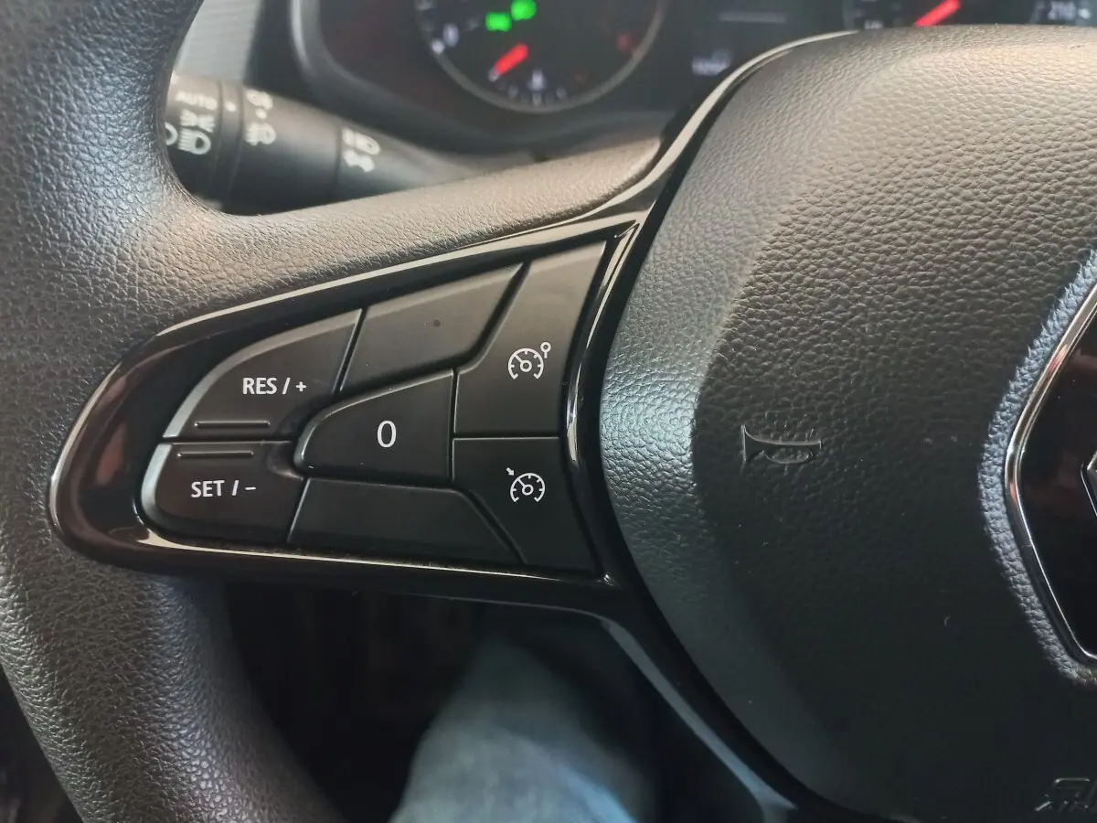 Gros plan sur les commandes du régulateur de vitesse sur le volant noir du Renault Trafic Fourgon blanc.