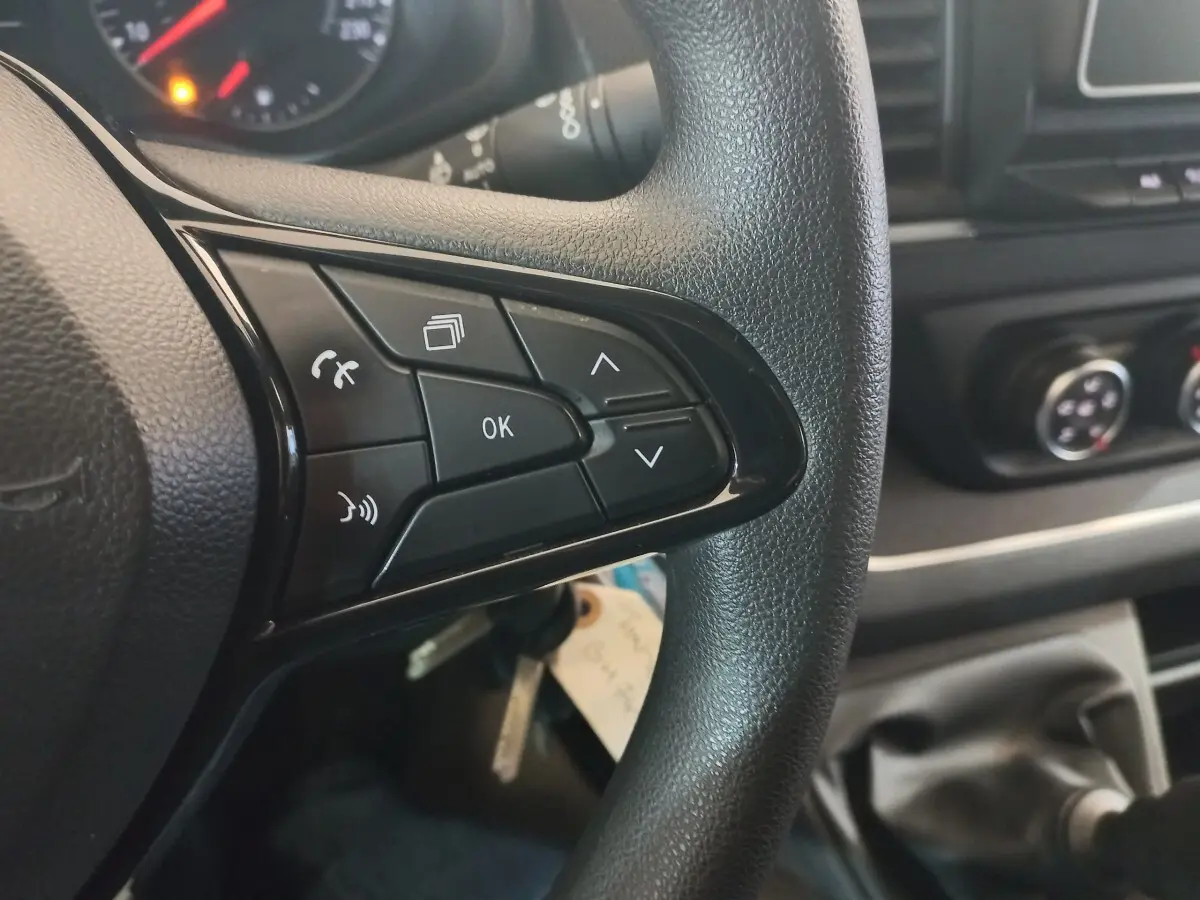 Gros plan sur les commandes multifonctions du volant noir du Renault Trafic Fourgon blanc, avec tableau de bord en arrière-plan.
