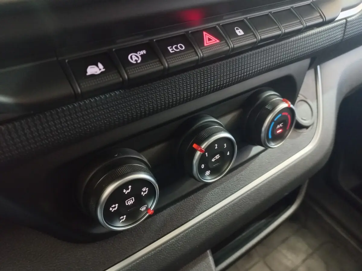 Gros plan sur les commandes de climatisation et boutons de fonction du tableau de bord du Renault Trafic Fourgon blanc.