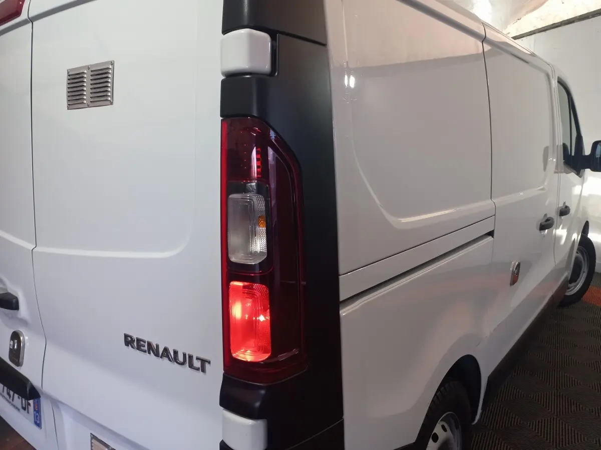 Vue arrière côté gauche du fourgon blanc Renault Trafic FG GCF L1H1 3T avec feu arrière allumé et logo visible.