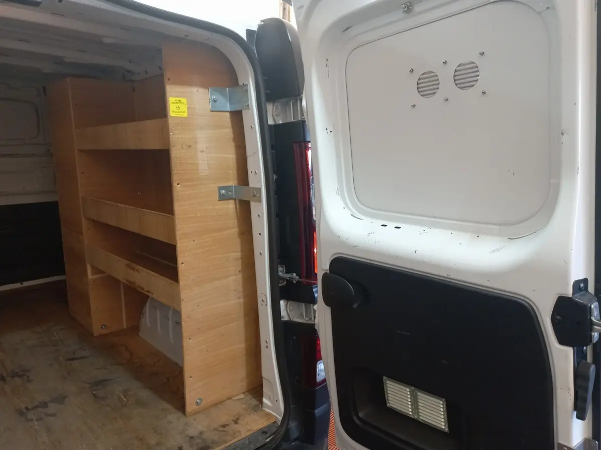 Vue arrière ouverte du Renault Trafic Fourgon blanc avec étagères en bois intégrées dans l'espace de chargement.