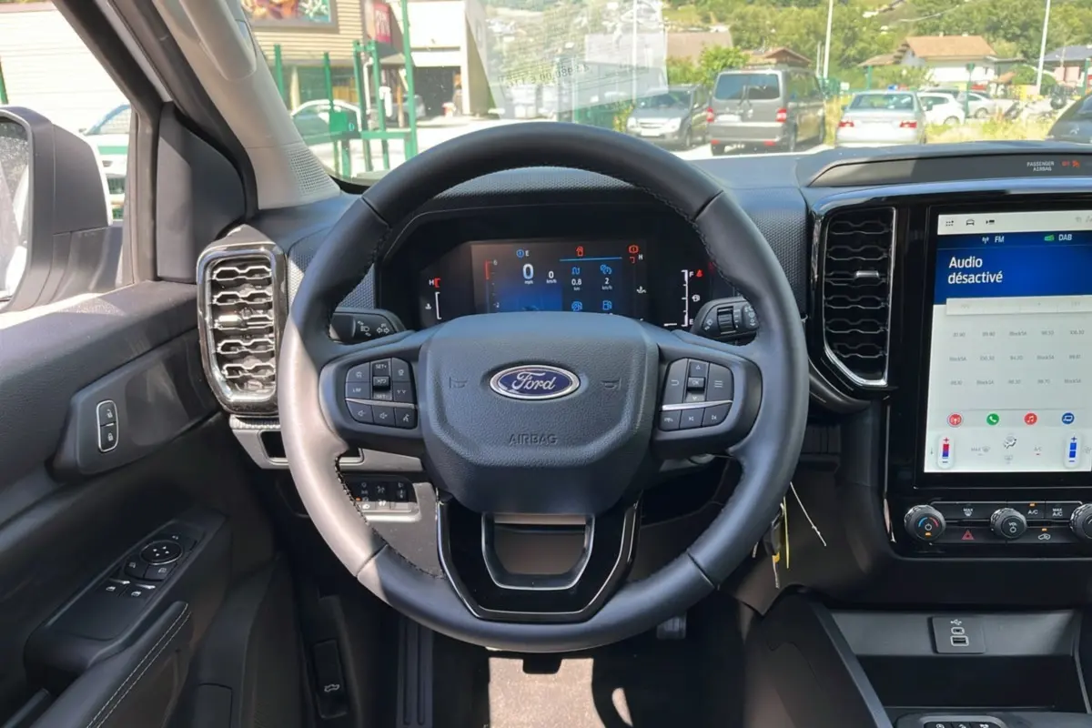 Vue intérieure centrée sur le volant cuir multifonctions du Ford Ranger 2025, avec écran tactile et tableau de bord numérique.