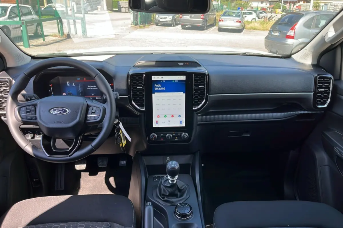 Vue intérieure avant du Ford Ranger 2025 blanc glacier, volant cuir multifonctions et écran tactile vertical central.