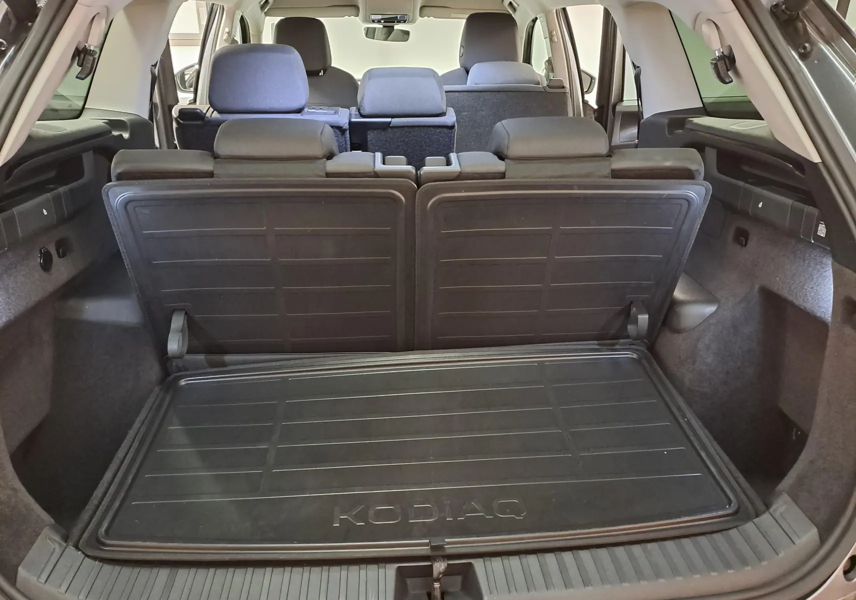 Vue arrière du coffre ouvert du Skoda Kodiaq gris graphite 2025, montrant les sièges rabattables et tapis de coffre KODIAQ.