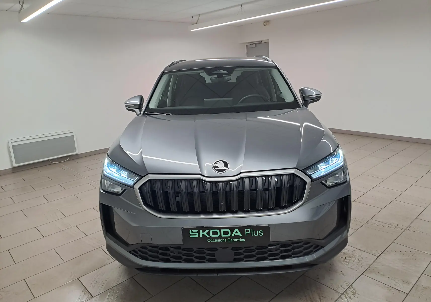Vue frontale d'un Skoda Kodiaq 2025 gris graphite avec phares LED allumés et calandre noire distinctive.