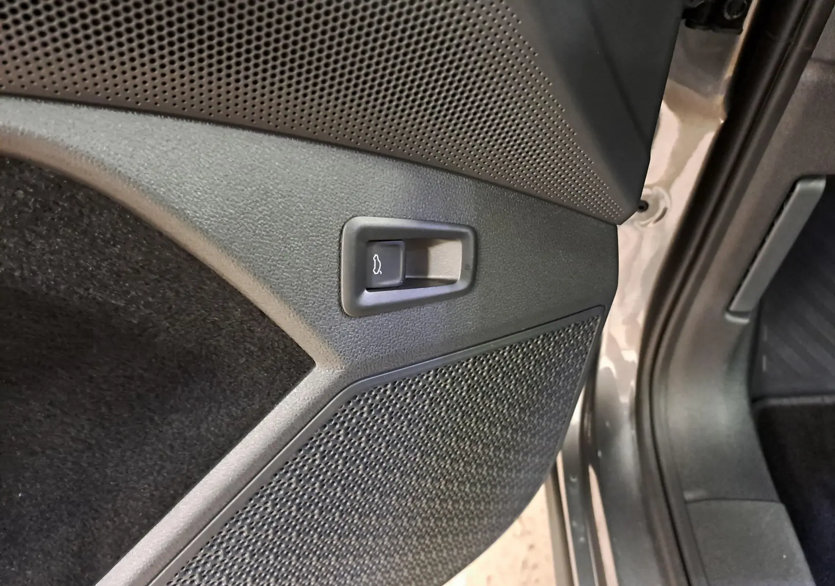 Détail du bouton d'ouverture du coffre sur la porte intérieure côté droit d'un Skoda Kodiaq gris graphite 2025.