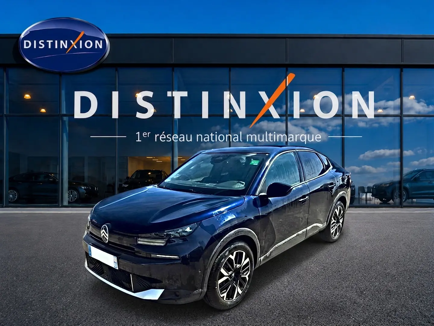 Citroën C4 X bleu en 3/4 avant droit, avec jantes alu et calandre distinctive, devant une vitrine Distinxion.