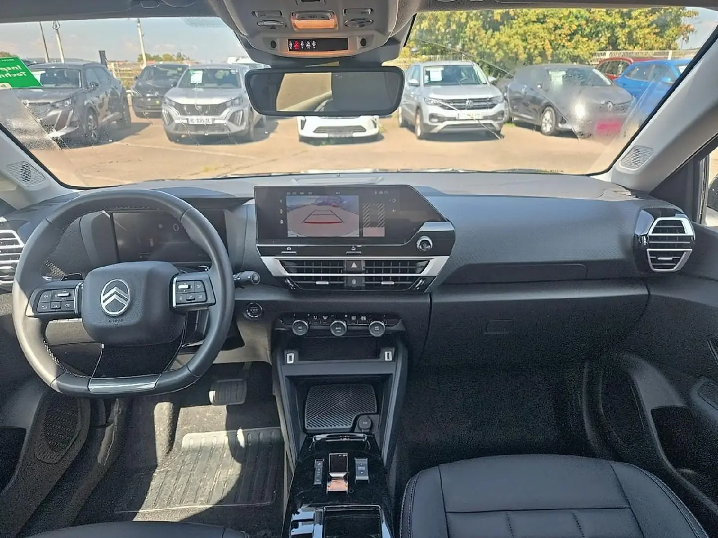 Vue intérieure avant du tableau de bord et volant cuir noir de la Citroën C4 X 1.2 hybride 2025 avec écran tactile et caméra de recul affichée.
