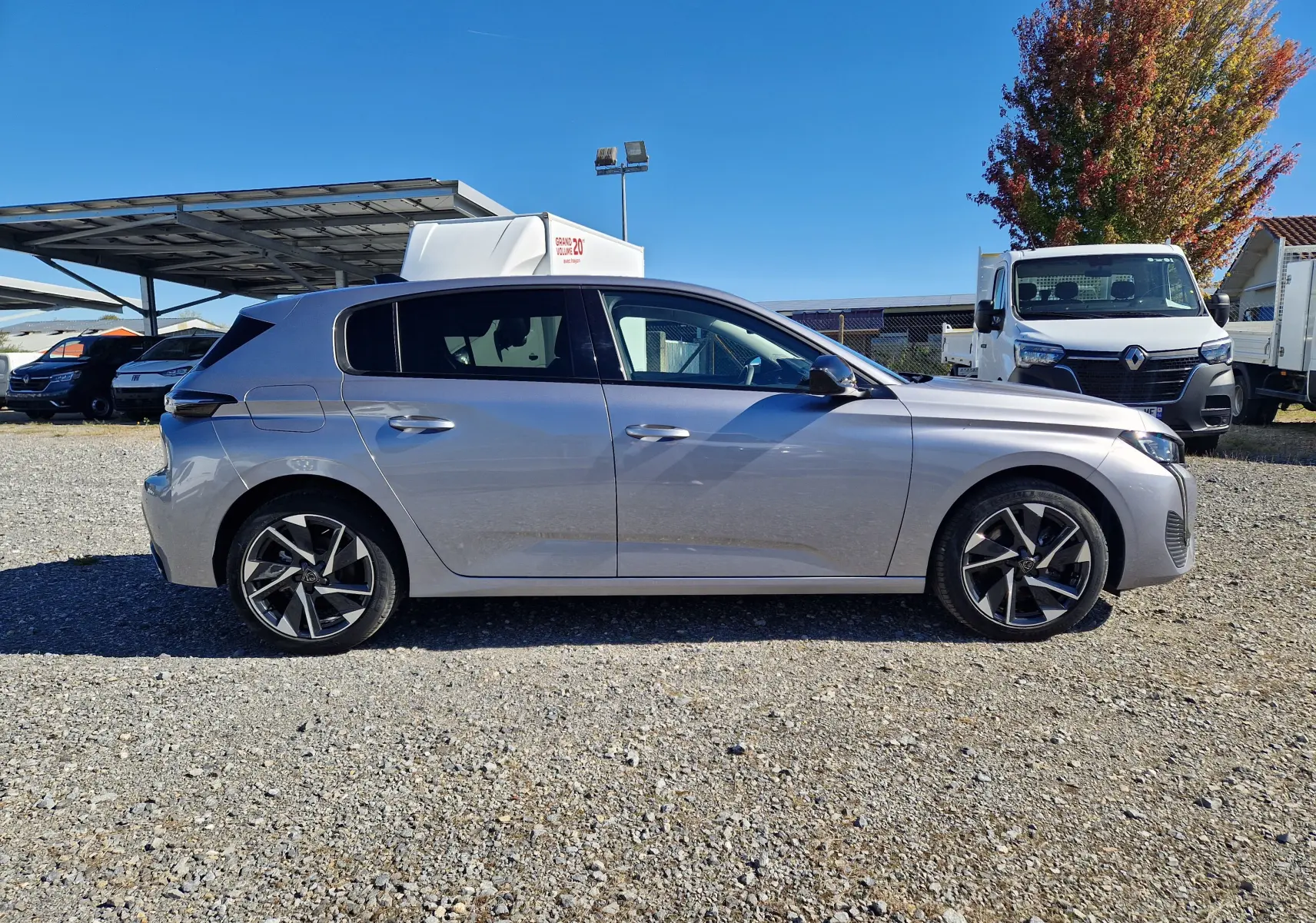 Peugeot 308 1.2 Hybrid 145 en gris Artense vue de profil côté gauche sur un sol gravillonné, avec jantes alliage.