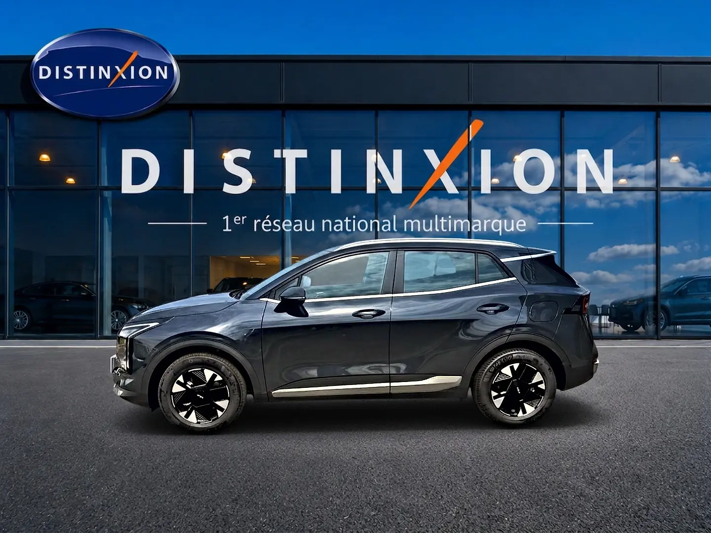 Vue latérale droite d'un KIA SPORTAGE 1.6 hybride gris eclipse avec jantes alu noires et barres de toit visibles.