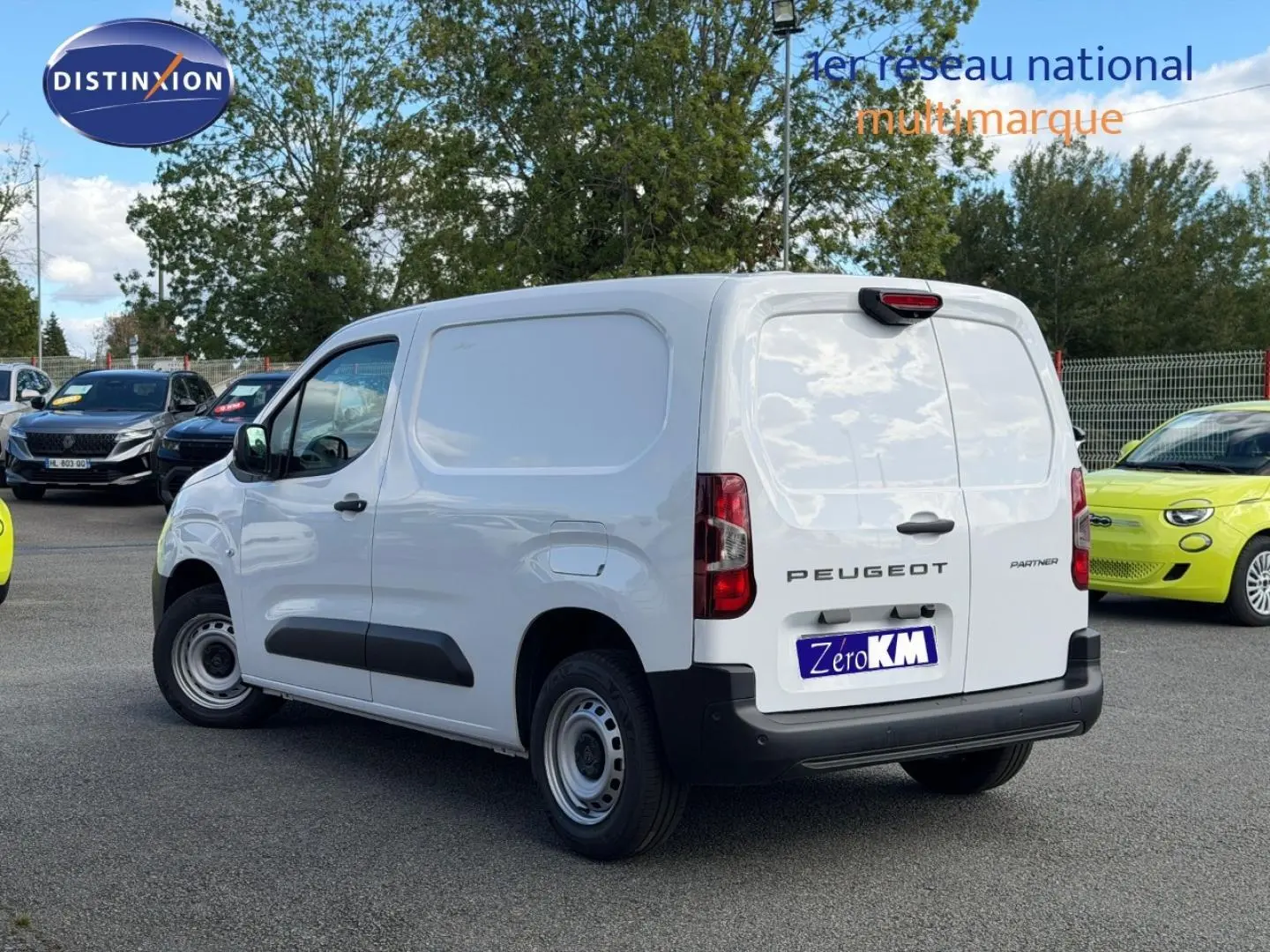 Vue 3/4 arrière droite d'un Peugeot Partner blanc Icy utilitaire avec porte latérale coulissante, en extérieur sur parking.