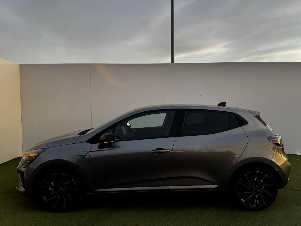 Profil côté gauche d'une Renault Clio V hybride gris schiste avec jantes noires et vitres surteintées.