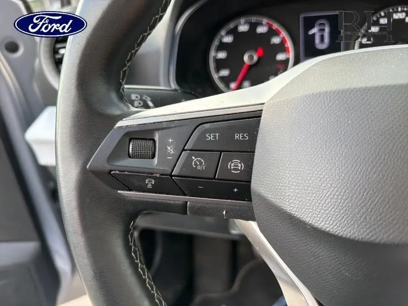 Gros plan sur les commandes au volant en cuir d'une SEAT ARONA gris urbain, avec tableau de bord partiellement visible.