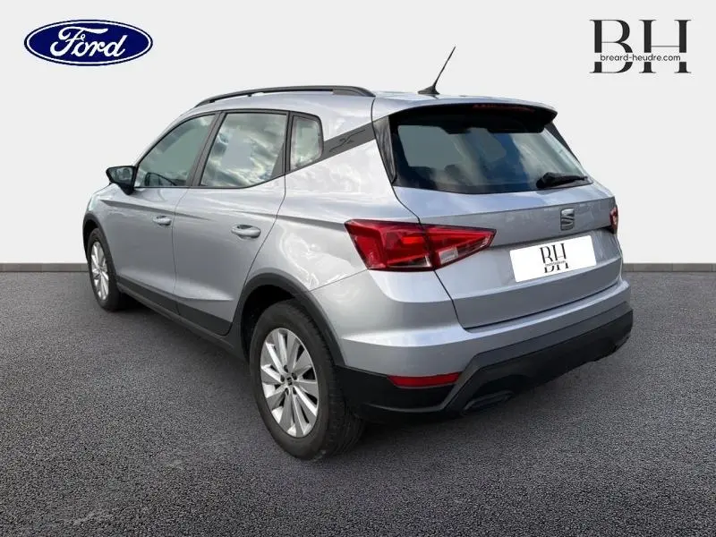Vue 3/4 arrière droite d'un SEAT ARONA gris urbain métal avec barres de toit et feux arrière LED visibles.