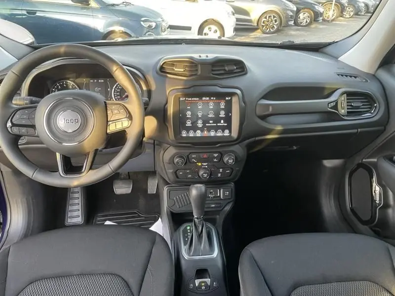 Vue intérieure avant du Jeep Renegade 2021 bleu Jetset Metal, montrant le tableau de bord noir avec écran tactile et volant multifonction.