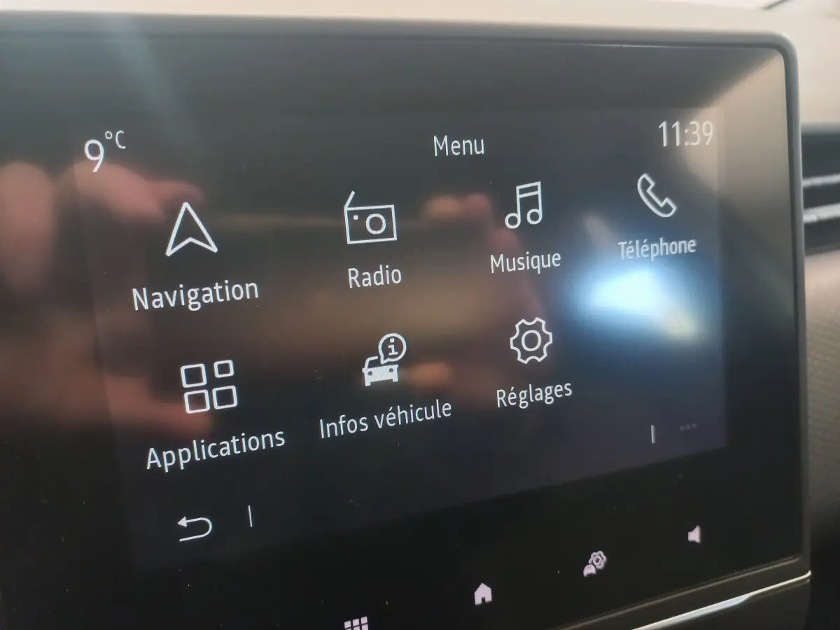 Écran tactile central de la Renault Clio Business blanc, affichant le menu principal avec navigation et musique.
