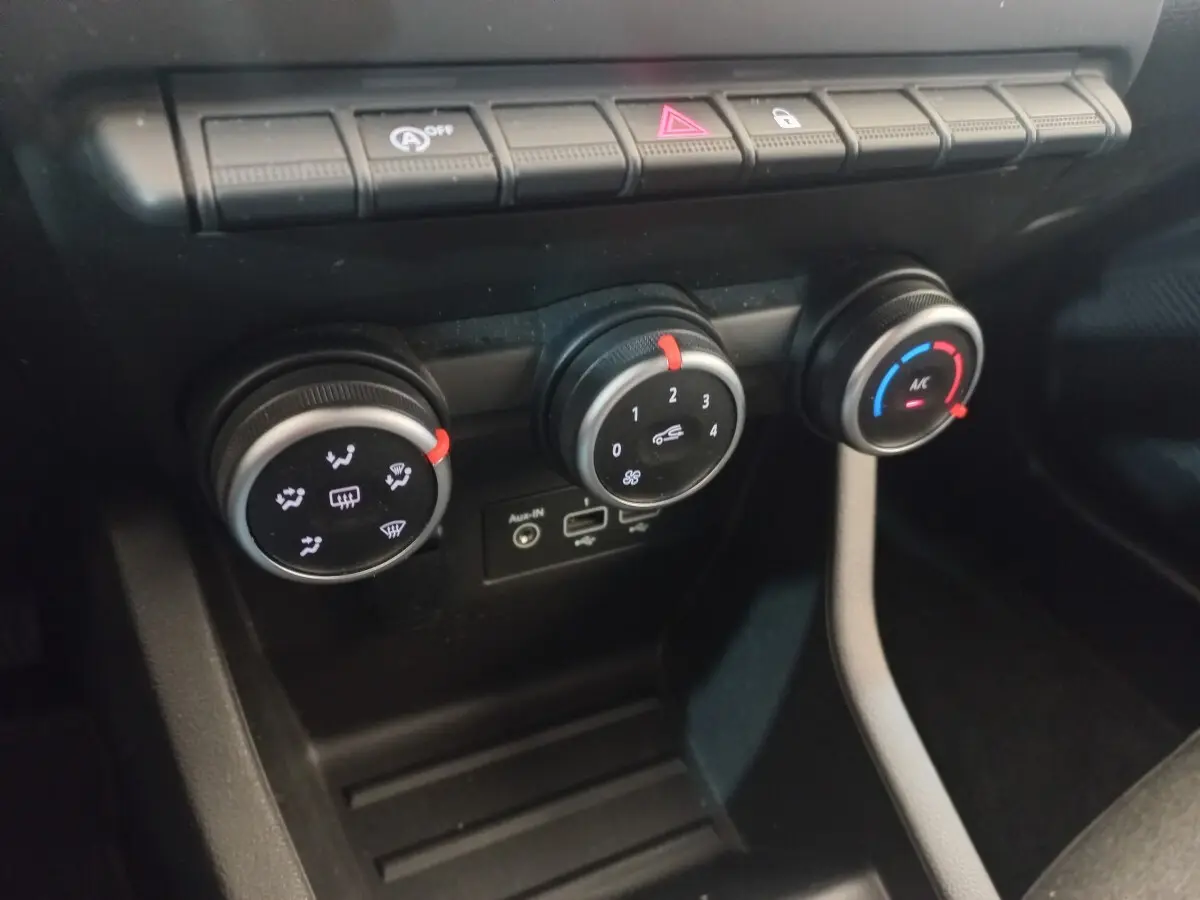 Gros plan sur les commandes de climatisation et ventilation noires de la Renault Clio Business blanche, avec boutons rotatifs et ports USB.