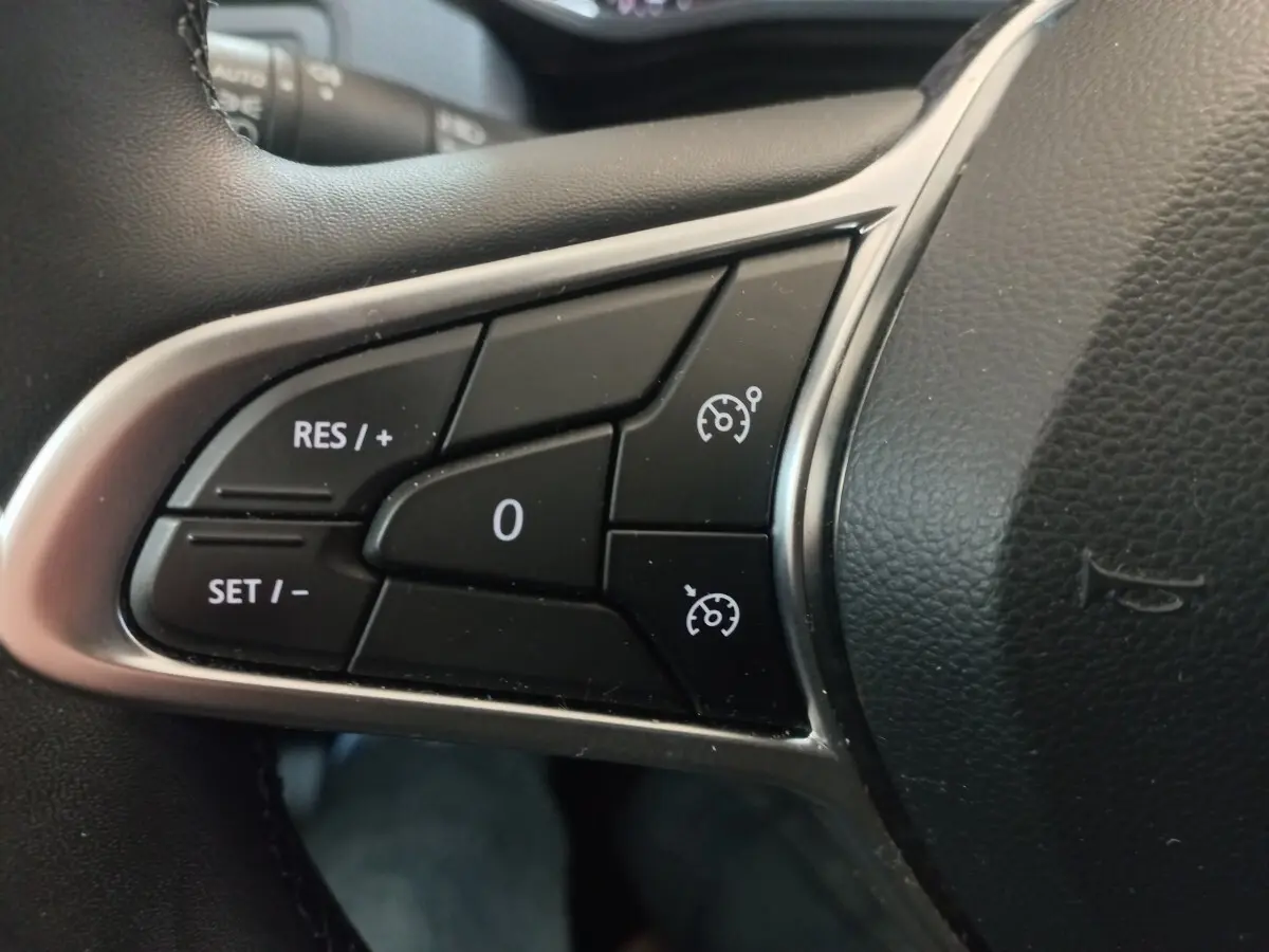 Gros plan sur les commandes de régulateur de vitesse à gauche du volant cuir noir de la Renault Clio Business blanche 2021.