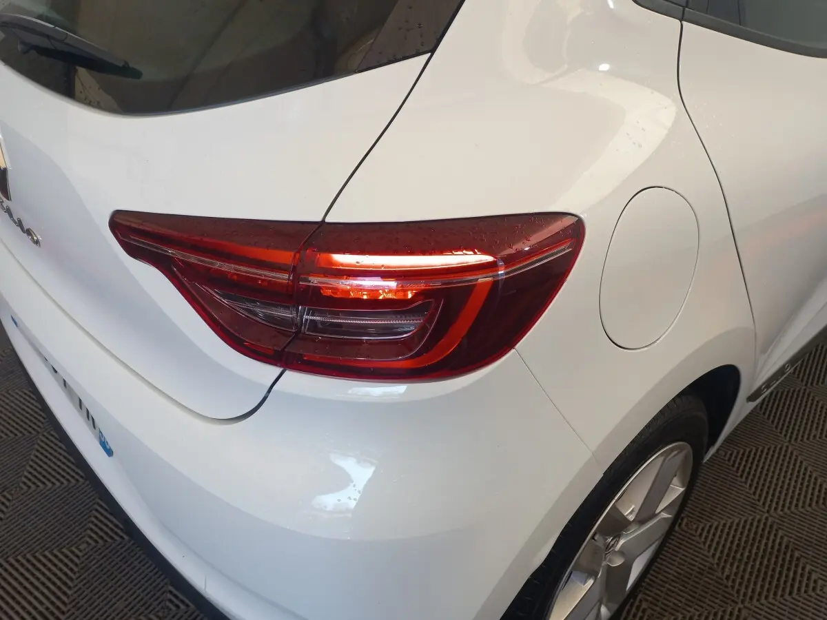 Vue 3/4 arrière droite d'une Renault Clio Business blanche, mettant en valeur le feu arrière LED et la trappe à carburant.