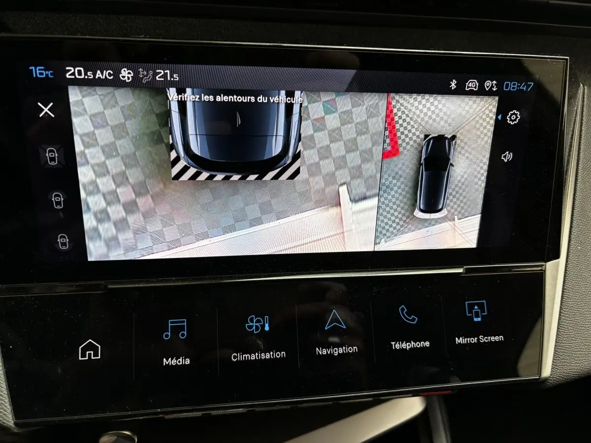 Écran tactile montrant l'aide au stationnement arrière avec vue 360° d'une Peugeot 308 blanche, tableau de bord moderne.